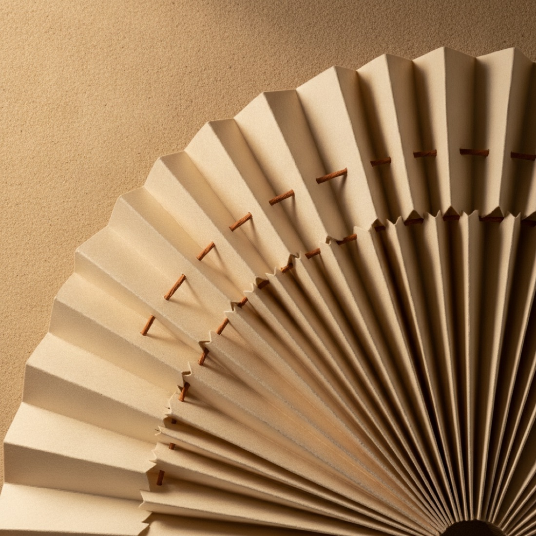 A folded paper hand fan stitched with copper thread