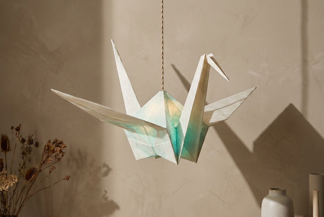 A watercolor-washed origami crane hanging in mid-flight